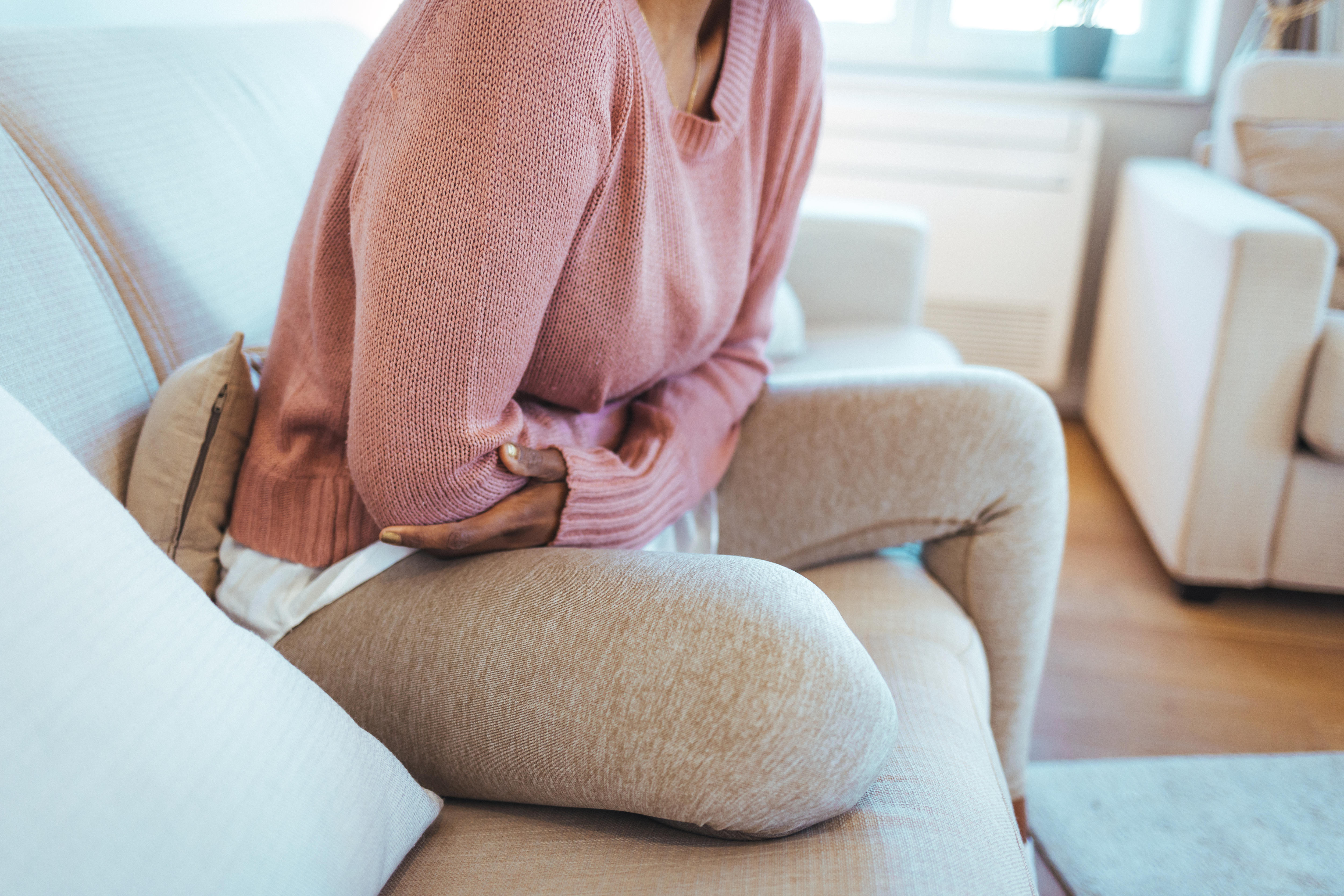 Woman holds her stomach while sitting on couch.