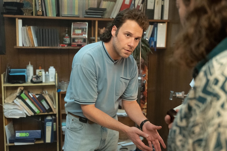 Seth Rogan in a clip from the TV series Pam & Tommy with a mullet, standing and indicating