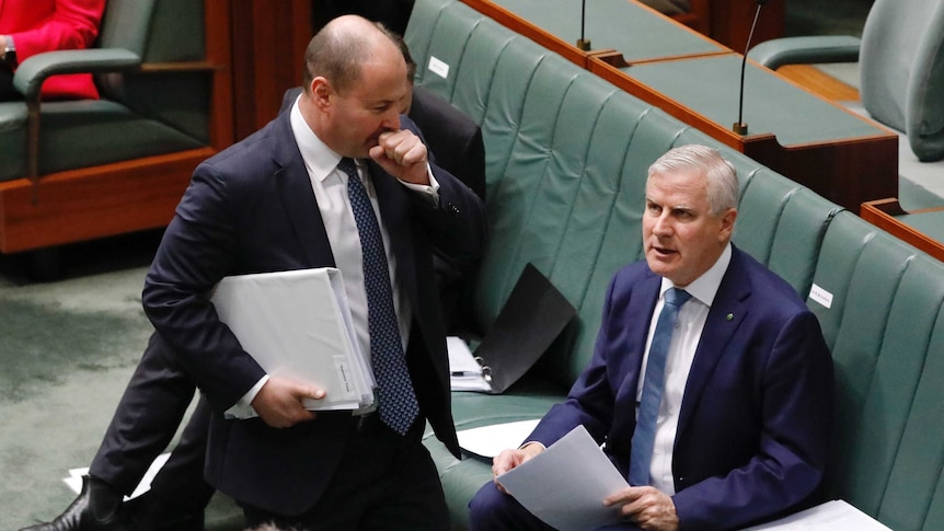 Walking into the House of Representatives, Treasurer Josh Frydenberg coughs into his hand as Deputy PM Michael McCormack watches
