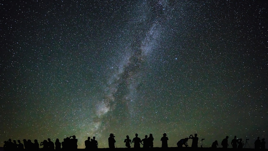 Image of a starry night sky, with silhouettes of people looking up at it.