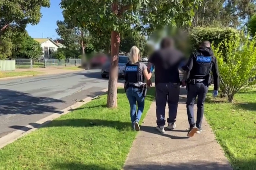 Two police officers take a man to a police car.