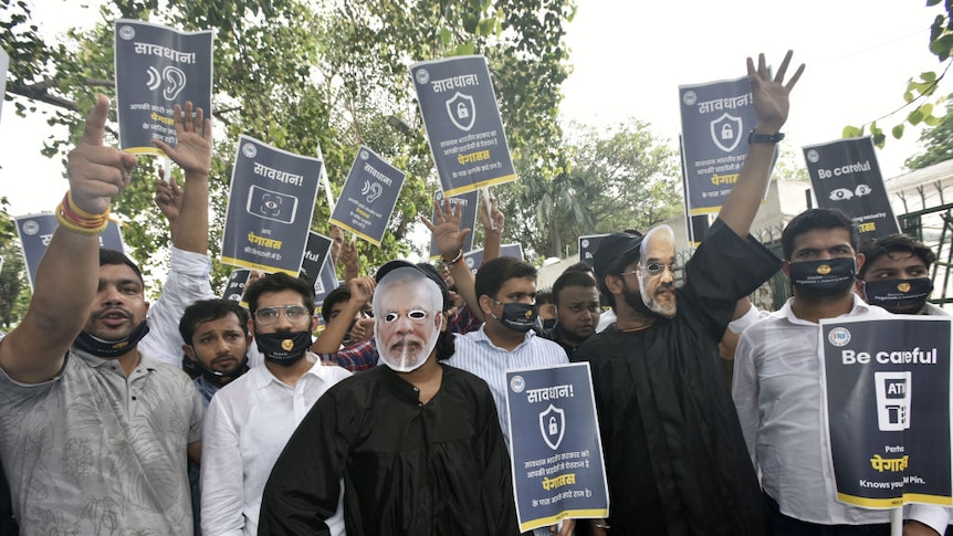 a group of protesters face the camera. some where masks of indian officials