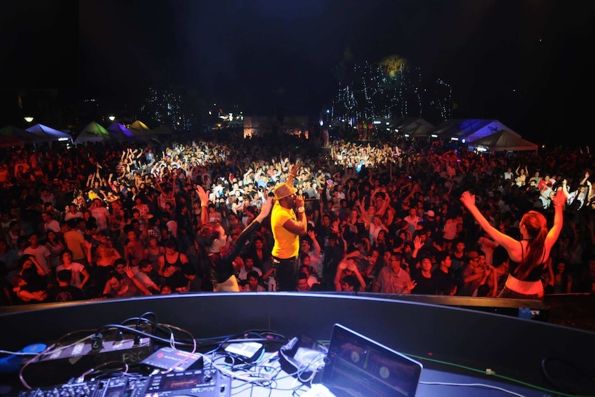 A DJ stand on a stage in a nightclub full of excited revellers.