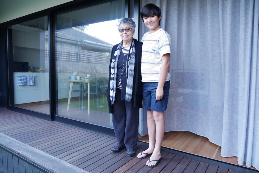 A grandmother and her grandson in front of their house