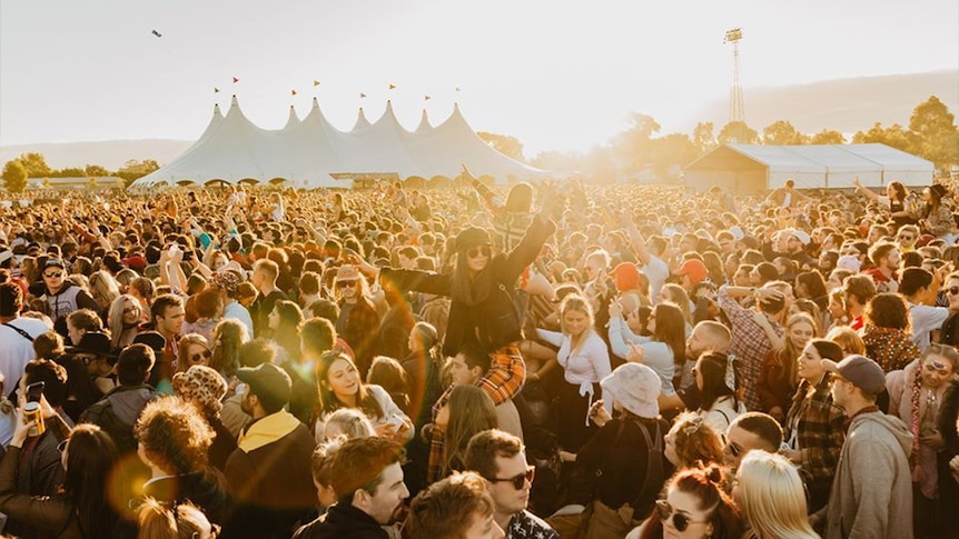 A crowd of people dance in the foreground, in front of a pavillion in the background.