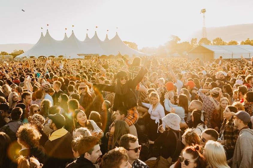 A crowd of people dance in the foreground, in front of a pavillion in the background.