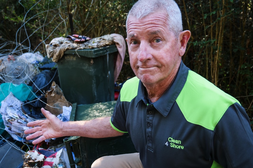 A man pointing to rubbish while looking at the camera.