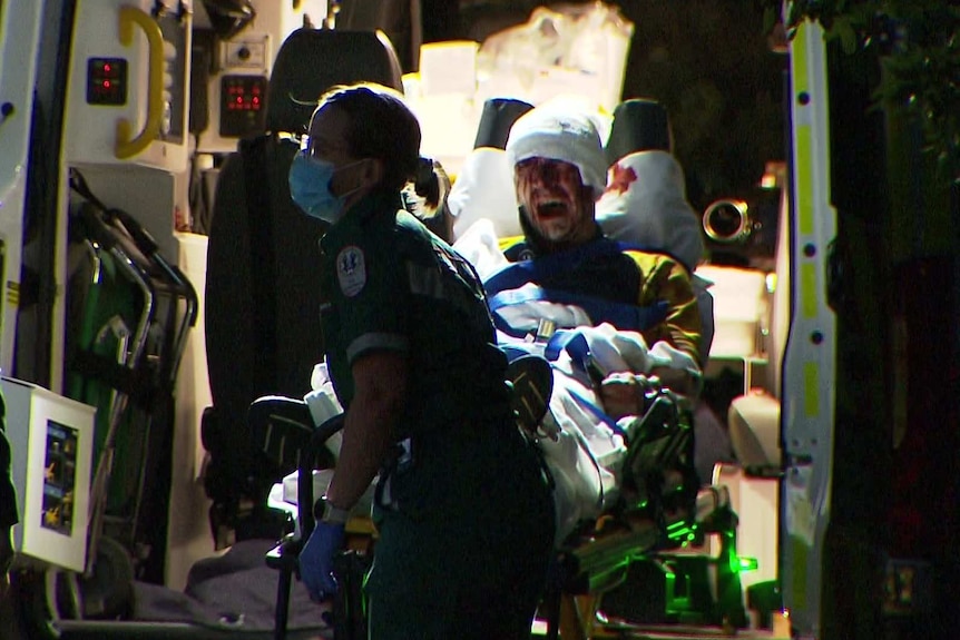 A man on an ambulance stretcher with his head bandaged.