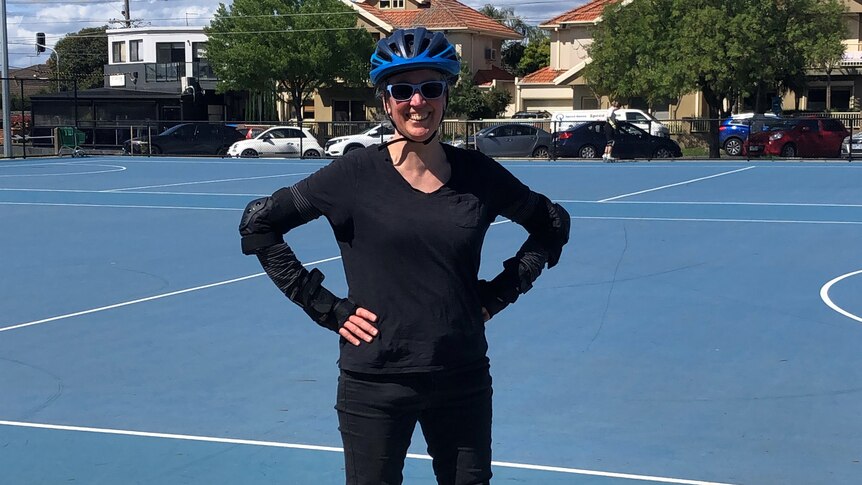 Hilary Harper wearing protective gear and rollerblades, on a basketball court.