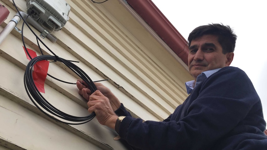 Clyde Juriansz holds a coiled internet cable taped to the side of his houses, meant to replace a severed broadband cable.