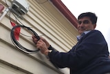 Clyde Juriansz holds a coiled internet cable taped to the side of his houses, meant to replace a severed broadband cable.