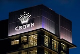 Tall buildings in the dark with lights on with an illuminated sign with the word Crown below a crown symbol.