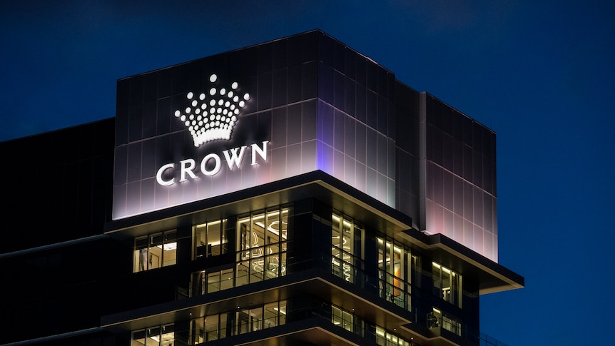 Tall buildings in the dark with lights on with an illuminated sign with the word Crown below a crown symbol.