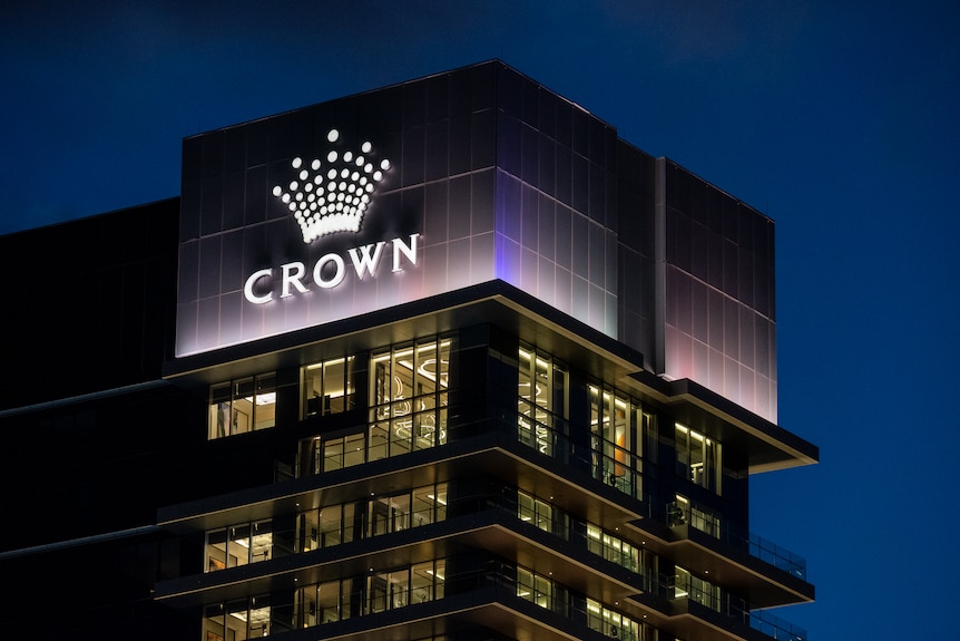 Tall buildings in the dark with lights on with an illuminated sign with the word Crown below a crown symbol.