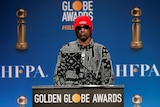 Snoop Dogg wearing a red beanie and black and white shirt and sunglasses at a lectern
