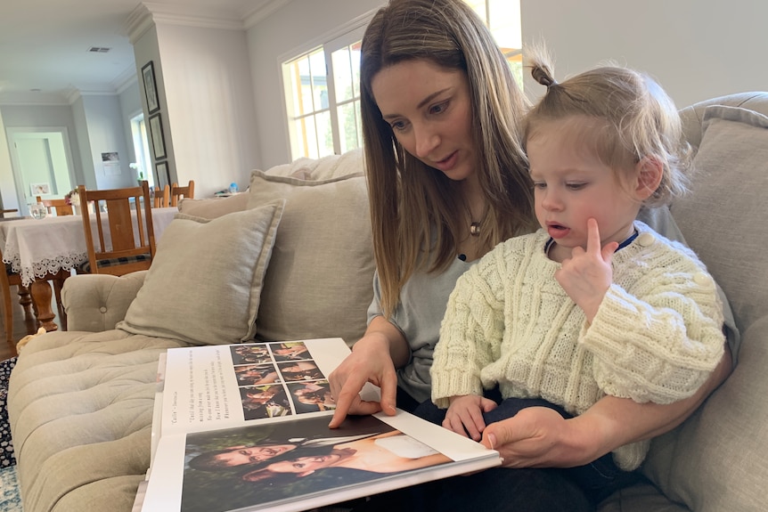 A young woman holding her young child while sitting on the couch and looking at photos