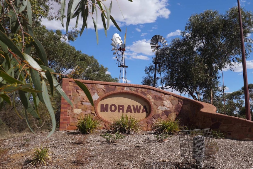 A stone wall with a Morawa entry signage in front of two windmills at the entrance to Morawa.