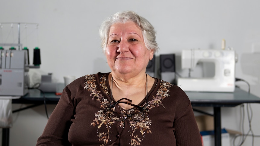 Nidaa Mustafa sits in a chair, smiling with a sewing machine in the background.