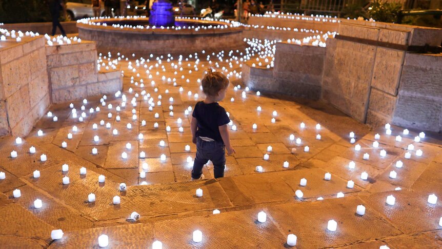 A child stands on steps surrounded by small white candles at night.