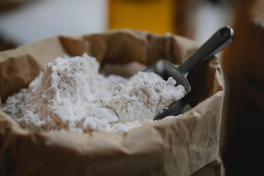 A paper bag filled with flour and a small metal scoop. 