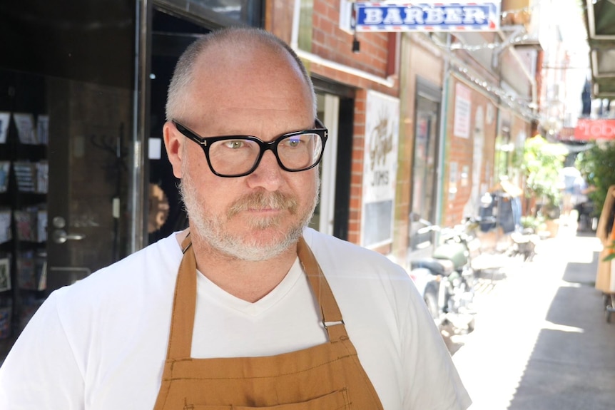 A man with short hair and black glasses look stern