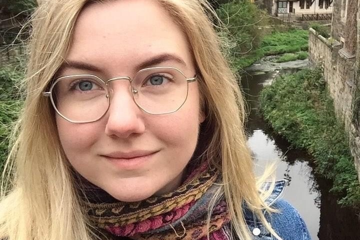 A selfie of a young woman with blonde hair standing on a bridge