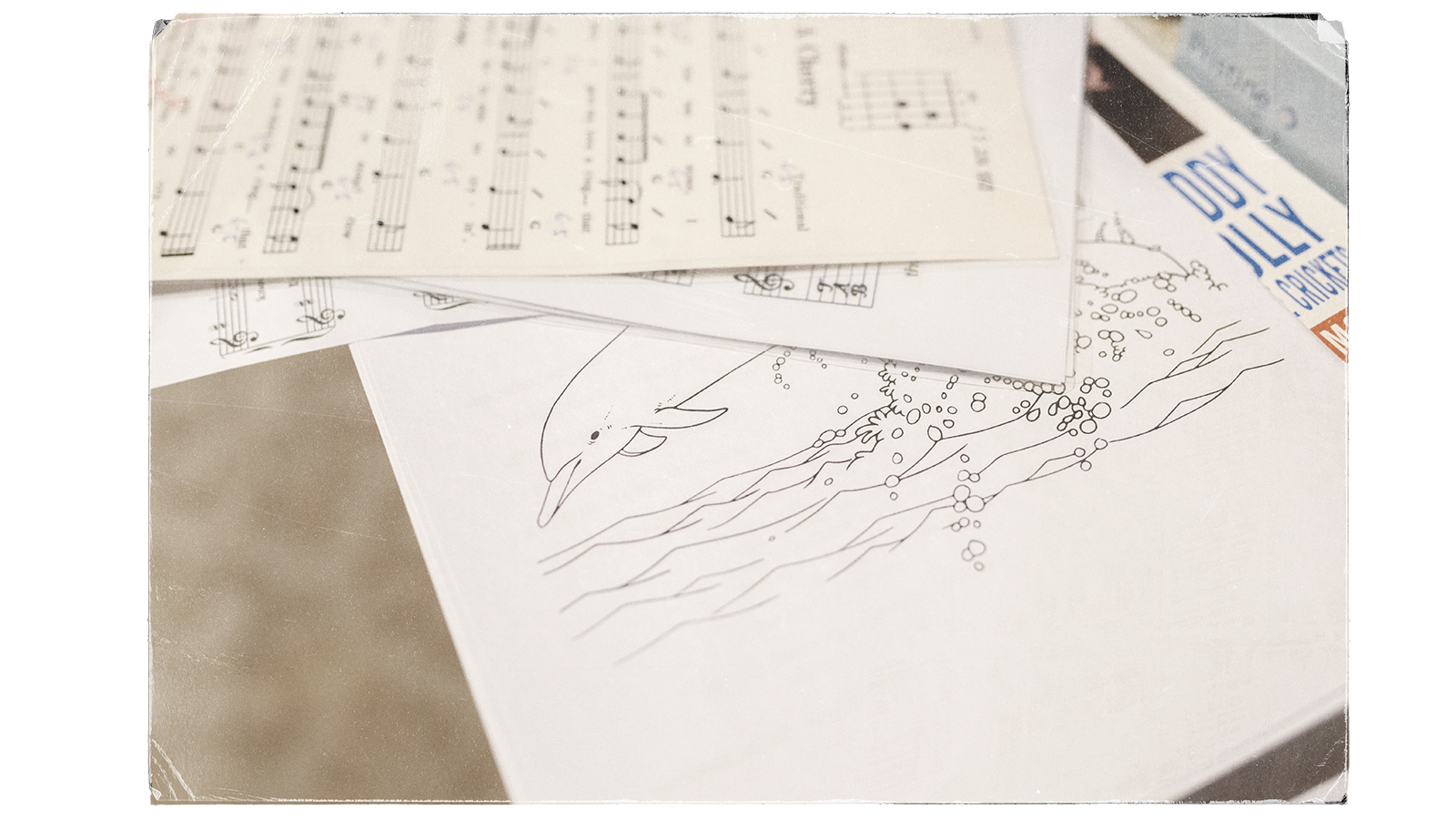 Sheets of music and a peice of paper with an illustration of a dolphin jumping out of water