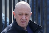 Yevgeny Prigozhin leaves a cemetery. He is bald and stares at the camera from a distance.