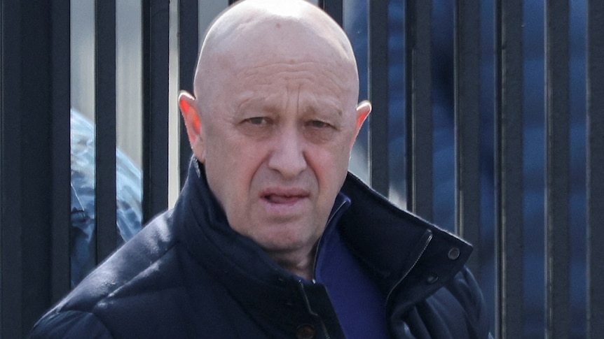 Yevgeny Prigozhin leaves a cemetery. He is bald and stares at the camera from a distance.