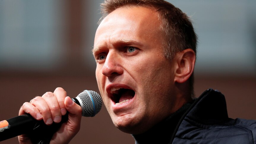 Alexei Navalny, a young man in a dark sports jacket, speaks into a microphone