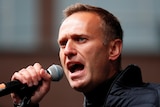 Alexei Navalny, a young man in a dark sports jacket, speaks into a microphone