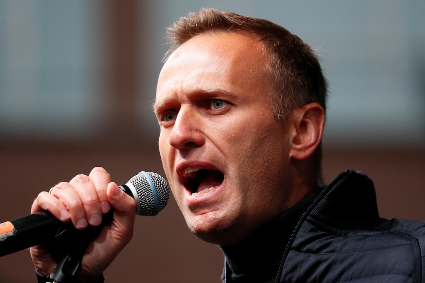 Alexei Navalny, a young man in a dark sports jacket, speaks into a microphone