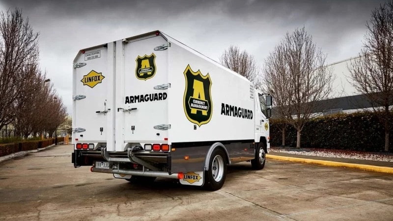 A white van carrying Armaguard's badge logo stationary in a parking lot.