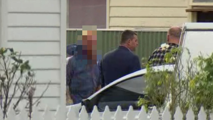 Man taken into police custody outside a house.