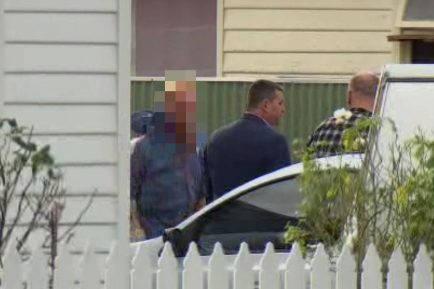 Man taken into police custody outside a house.