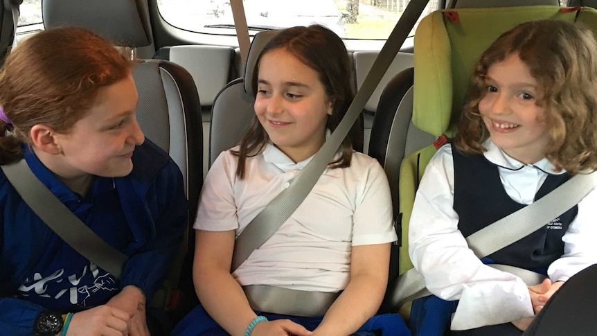 Three primary school-aged girls in the backseat of a car