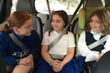 Three primary school-aged girls in the backseat of a car