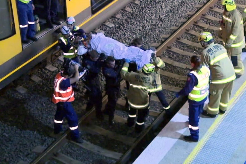 Fire and Rescue officers and police carry a man on a stretcher across railway tracks