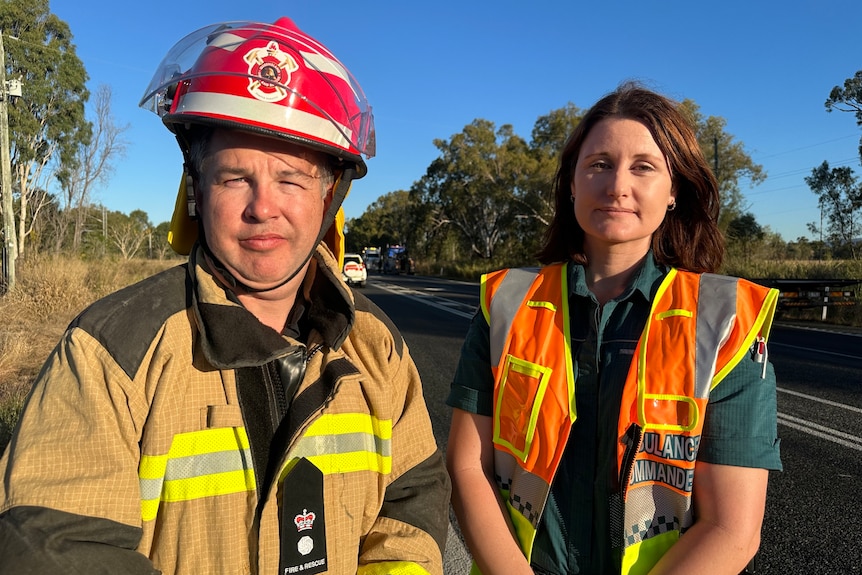 A fire fighter and a paramedic stand on the side a road