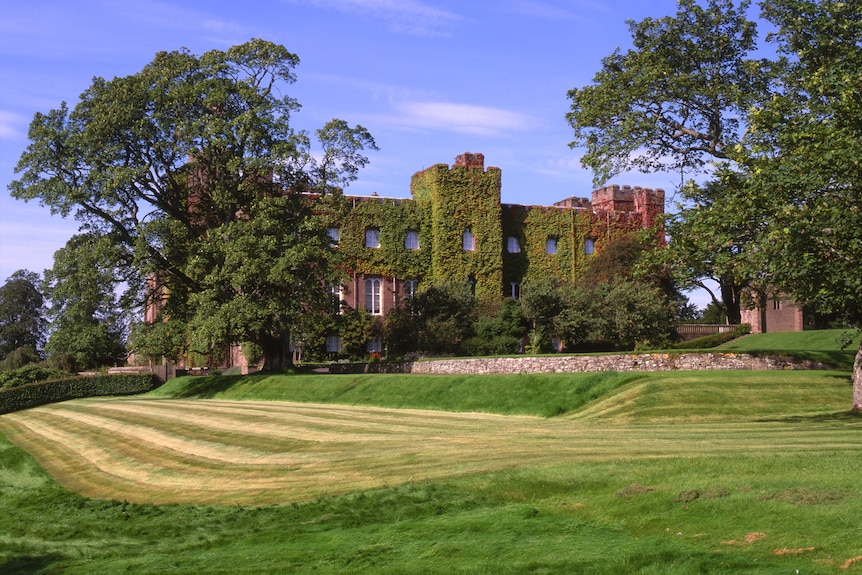 A vine-covered medieval palace surrounded by green fields and trees.