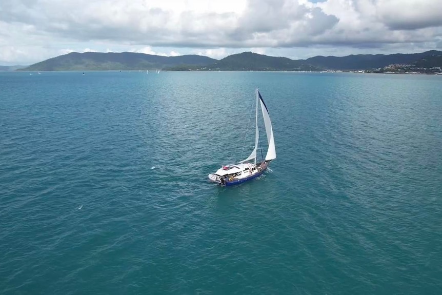 An aerial shot of a yacht, with land visible in the background