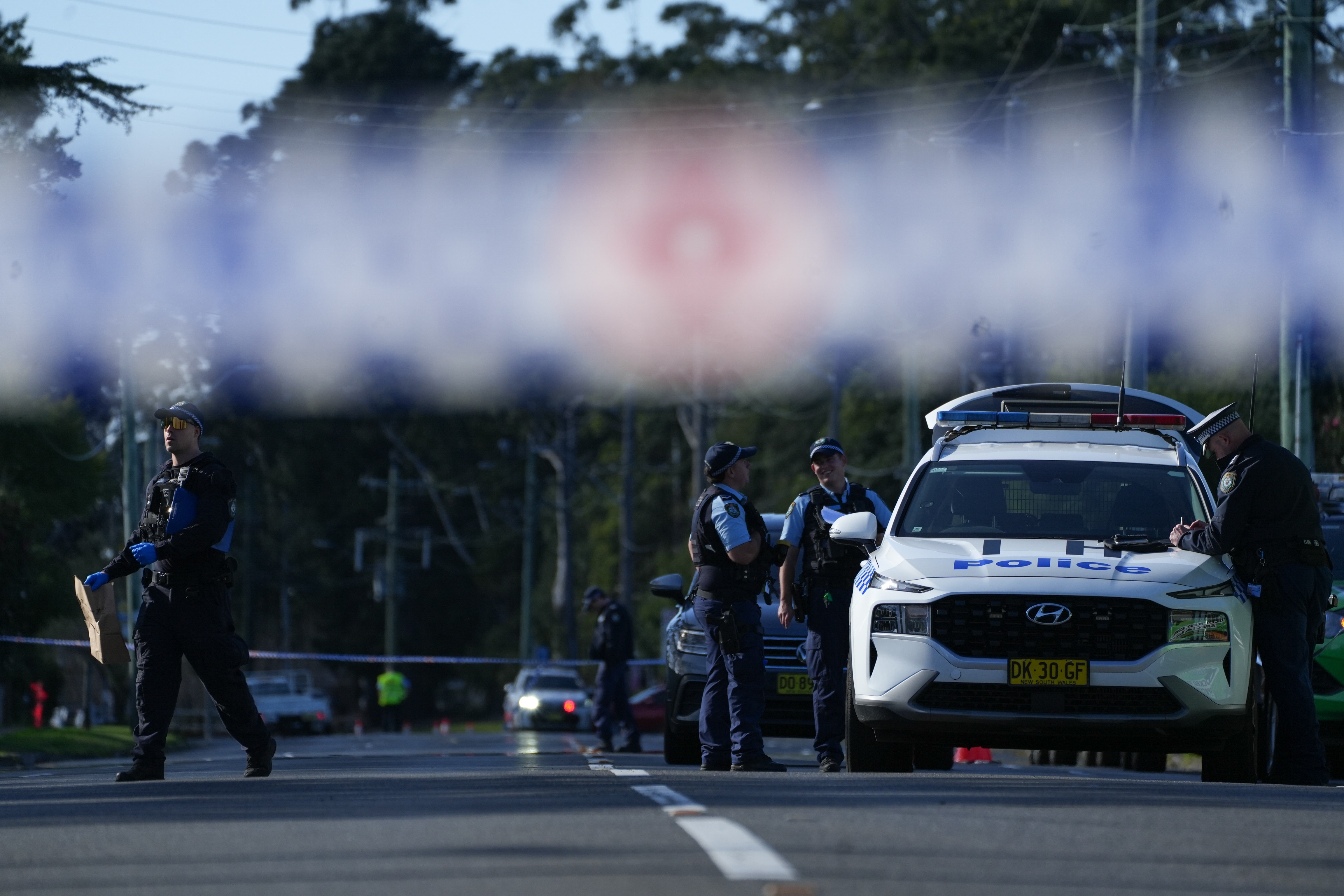 Police tape crosses the road where police cars are parked and police officers are talking to each other.