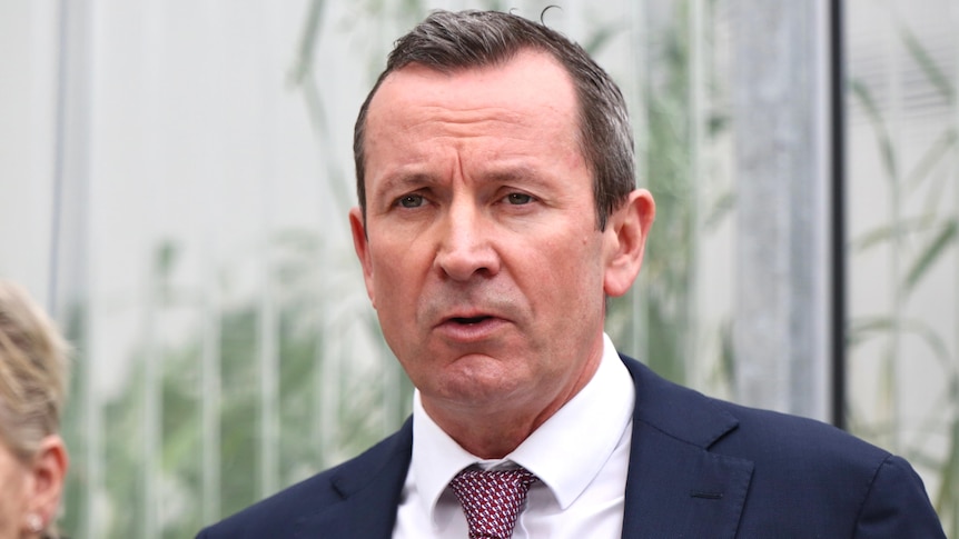 A middle-aged man with dark hair wearing a suit and tie speaks at a press conference.