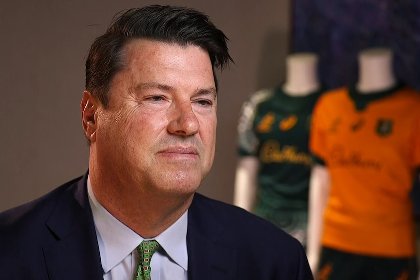 A man in a suit smiles in front of Wallabies jerseys