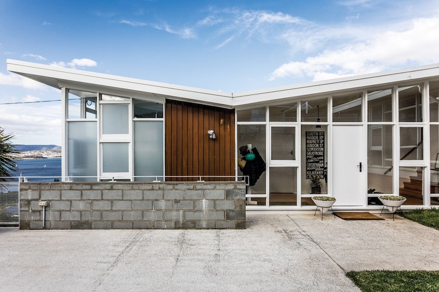 A wide shot of a house with a butteryfly roof, there is wood panelling on the outside and a wall of windows.