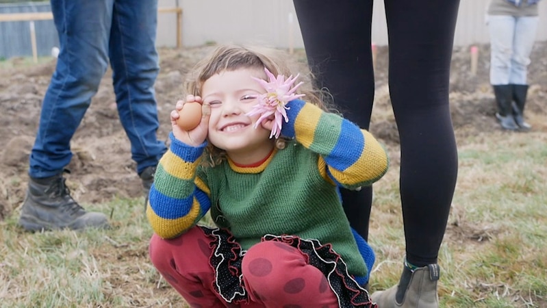 Young girl squatting down holding an egg and a flower up to her face