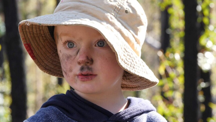 Preschool-age boy in burnt forest with charcoal smeared over his face