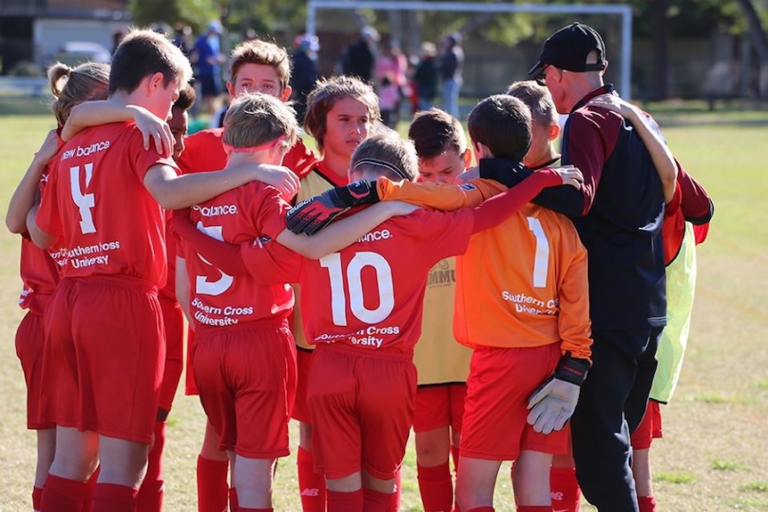 Young football players from the Southern Cross University academy huddle on the field with their coach