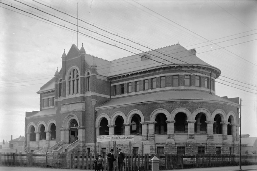 Black and white photo of historic Victorian building with adults and children standing outside.