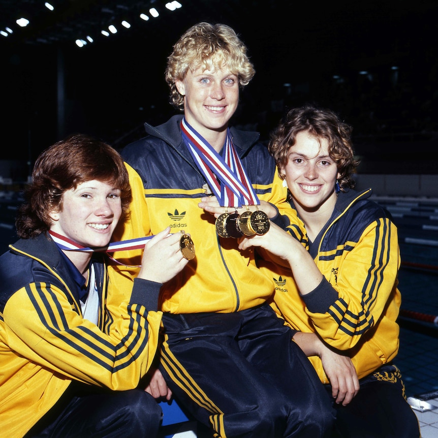 Three young women in green and gold tracksuits pose with their Commonwealth Games medals, smiling